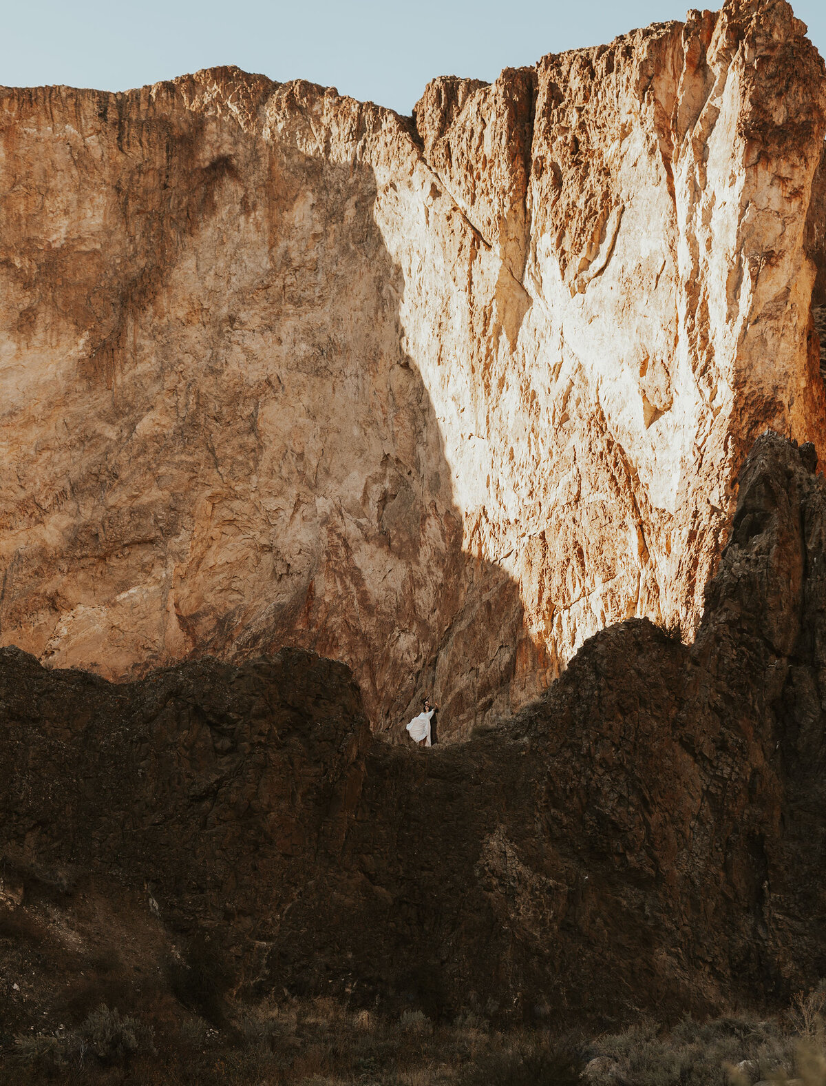 bride and groom stand in front of huge towering rocks among the golden sun in Moab, Utah