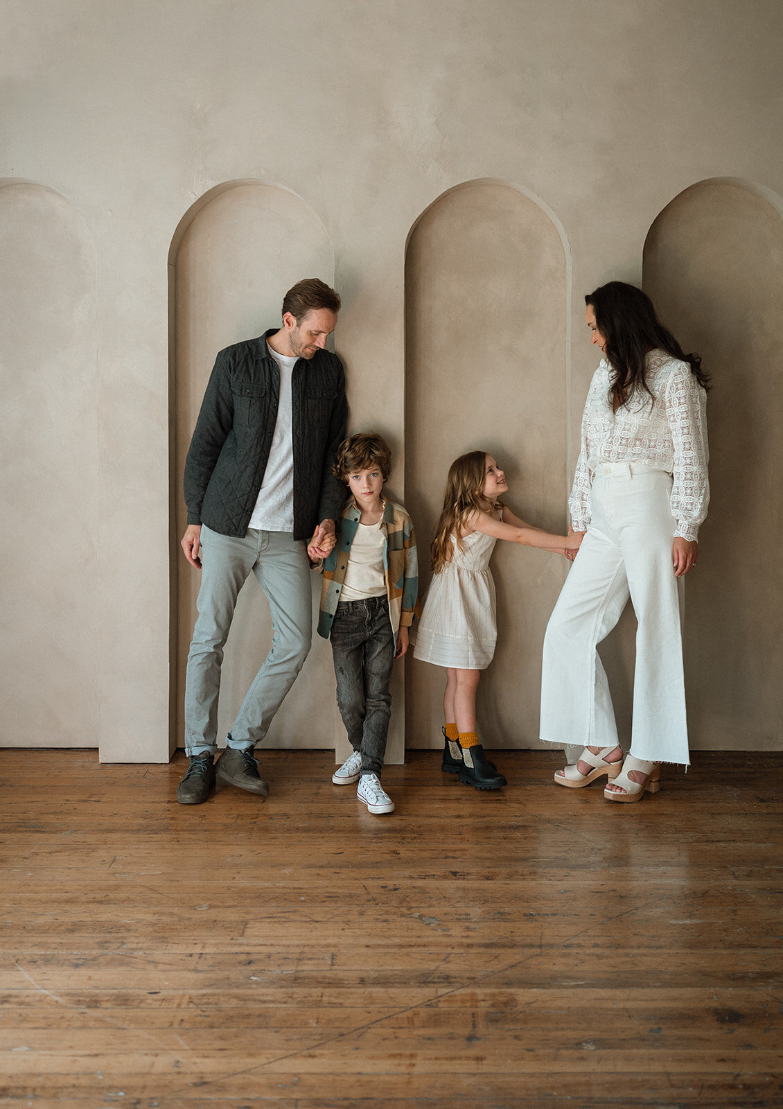 Family standing together with soft arches in the background
Parents smiling at each other in a modern studio with their two children running around them, natural light and warm neutrals.