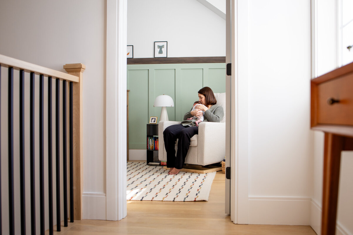 Looking into nursery from hallway and seeing mom snuggling baby girl in the rocker