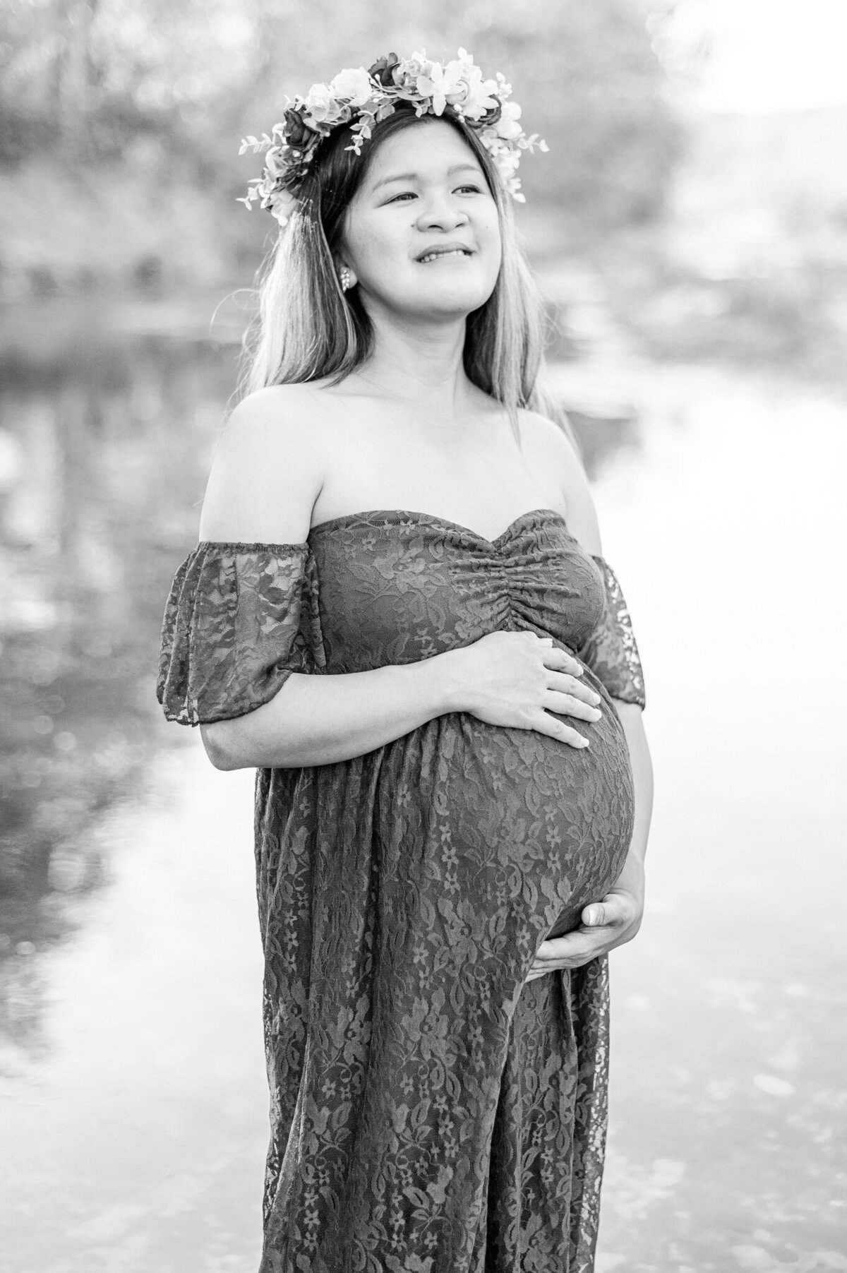 Black and white maternity portrait of a mama holding her bump and gazing off into the distance.