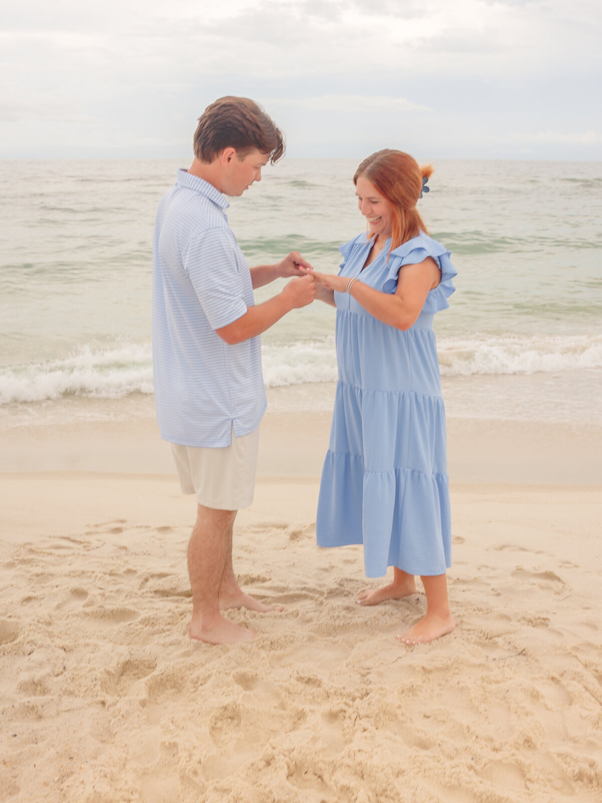 A groom-to-be placing the ring on his fiancée's finger  after a surprise proposal on the beach