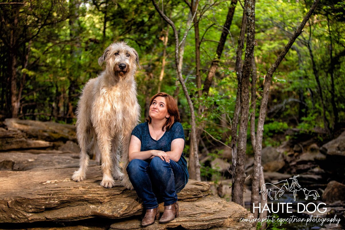 A woman sitting on a rock at Stone Creek Park in Flower Mound, looking up at an Irish Wolfhound dog with long, shaggy fur.