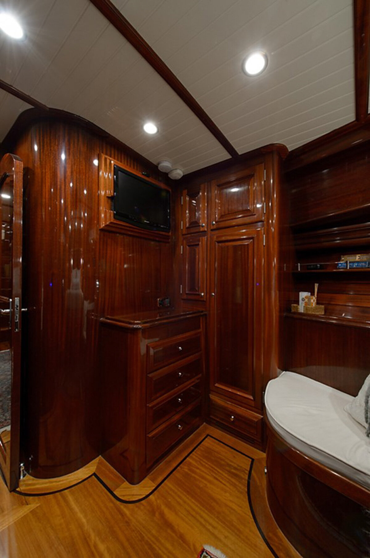 small room with glossy wooden walls and furnishings that has dresser with drawers, a built-in wardrobe, a flat-screen TV mounted above the dresser, and a cozy cushioned seating nook