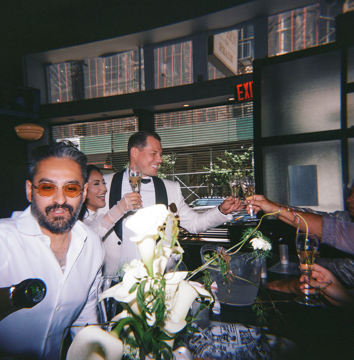 Flash film photo of newlyweds raising glasses with friends at a New York City bar after their elopement.