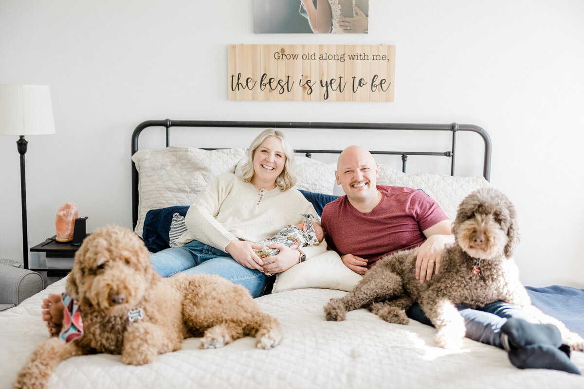 family snuggling on the bed with dogs and holding baby