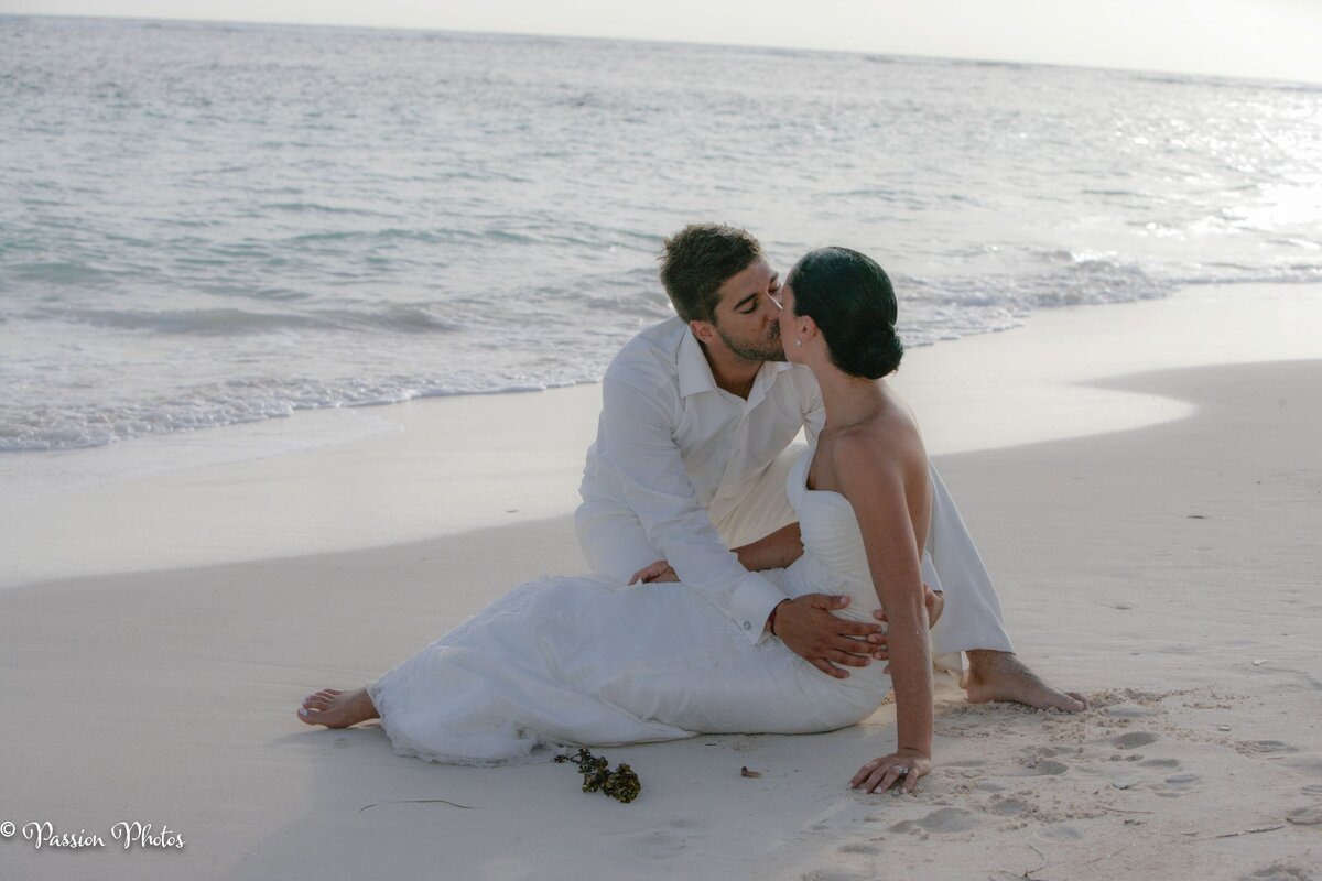 A couple shares a romantic kiss while sitting on a picturesque beach, with the waves gently lapping at the shore. This intimate moment highlights the beauty and romance of destination weddings, capturing the essence of love and adventure in stunning coastal settings.