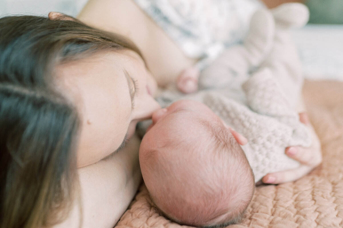 Mother cuddling with newborn baby on a bed by Oklahoma City Newborn Photographer Courtney Cronin