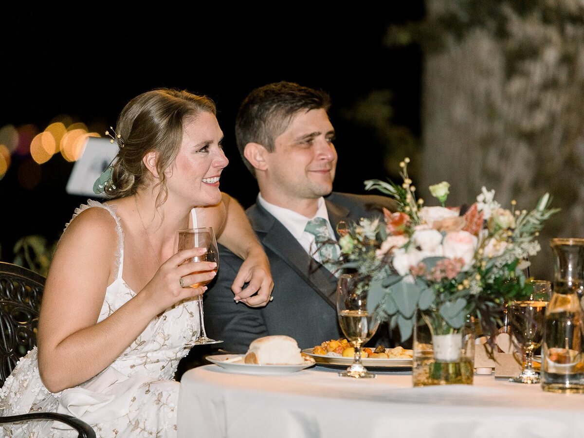 Bride and groom at their table during wedding reception with bouquet flowers in vase.
