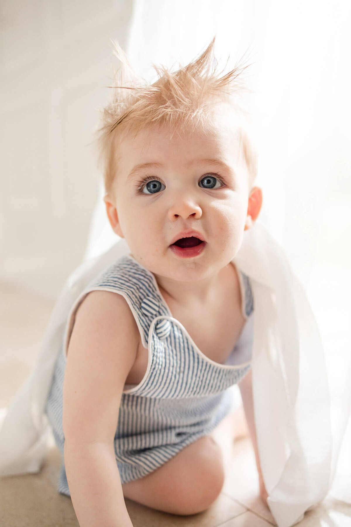 Cute baby boy peeking through white sheer curtains during Cleveland family photography session at home.