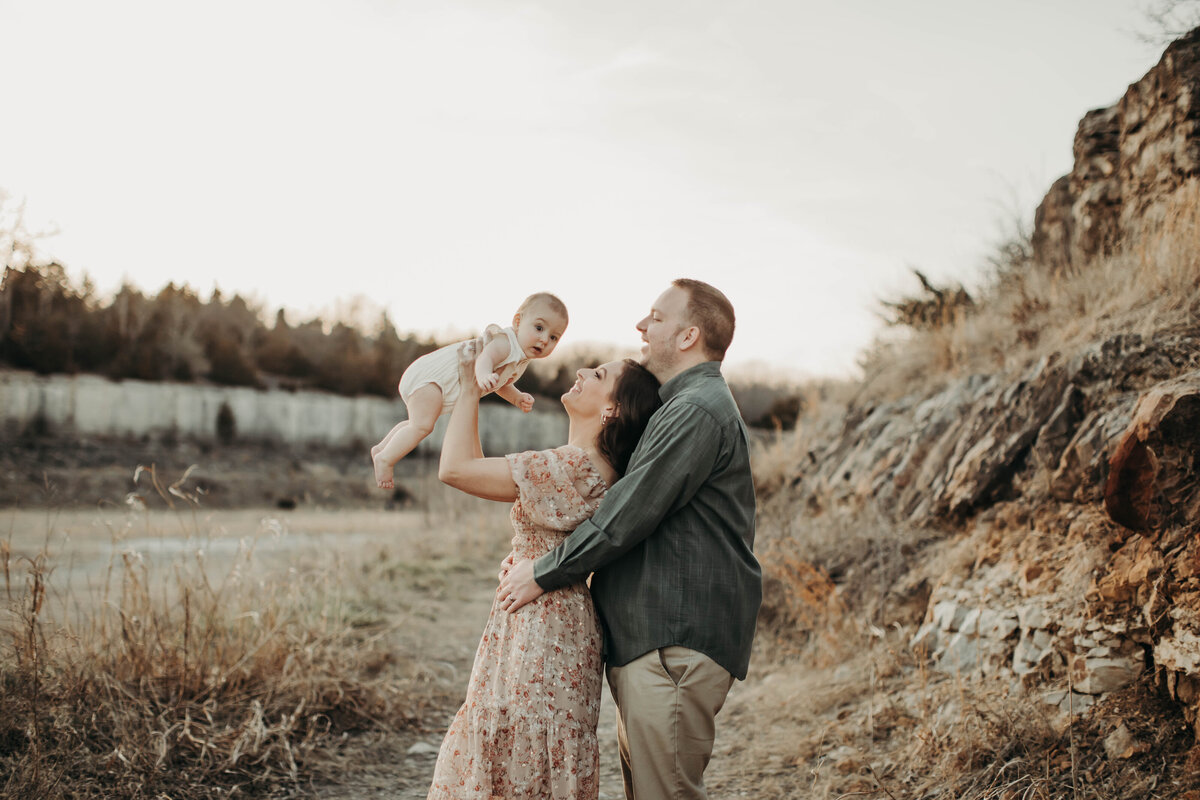 Candid moment of dad holding baby in the air as mom laughs beside him. 