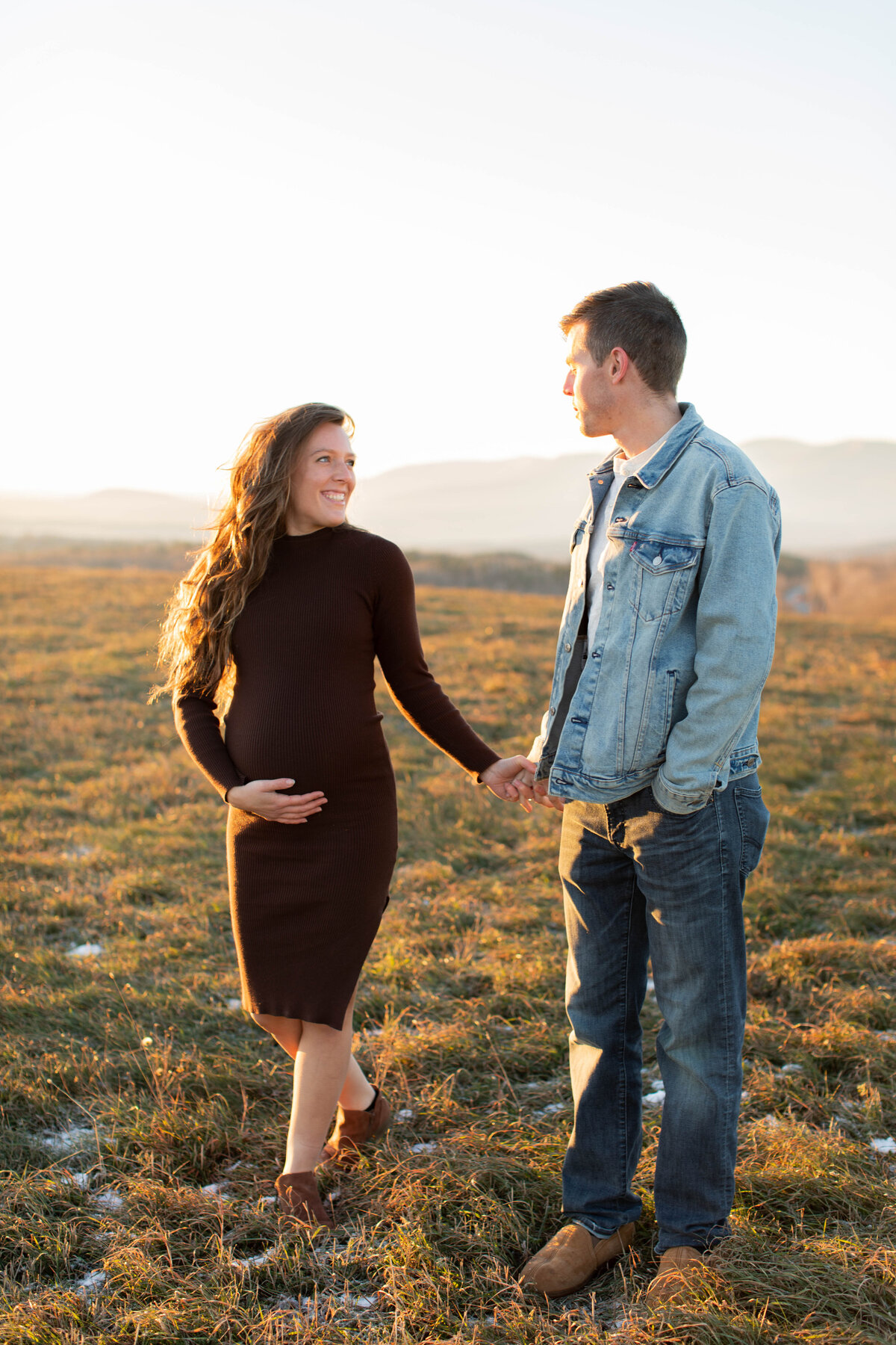 Pregnant couple walk hand and hand in a field at sunrise