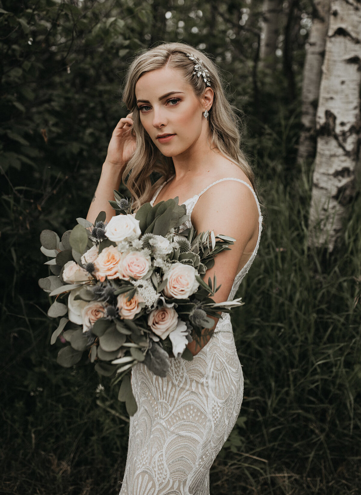 Gorgeous bride wearing detailed lace gown, and a stunning jewelled hairpiece, holding large bouquet of pink roses and stunning greenery, , captured by Ash Maclean Photography, romantic elopement and wedding photographer in Red Deer, Alberta. Featured on the Bronte Bride Vendor Guide.