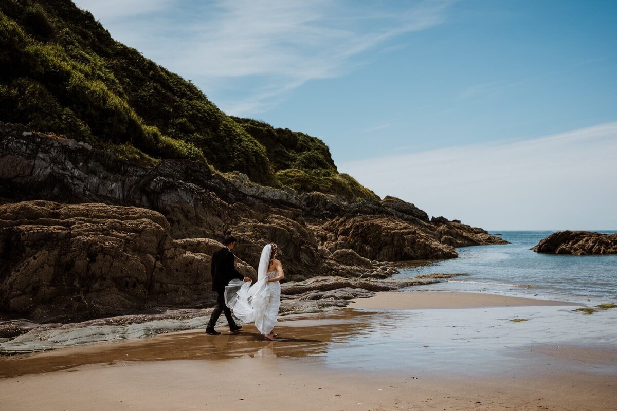 A bride and gorom walking on a beach towards the water