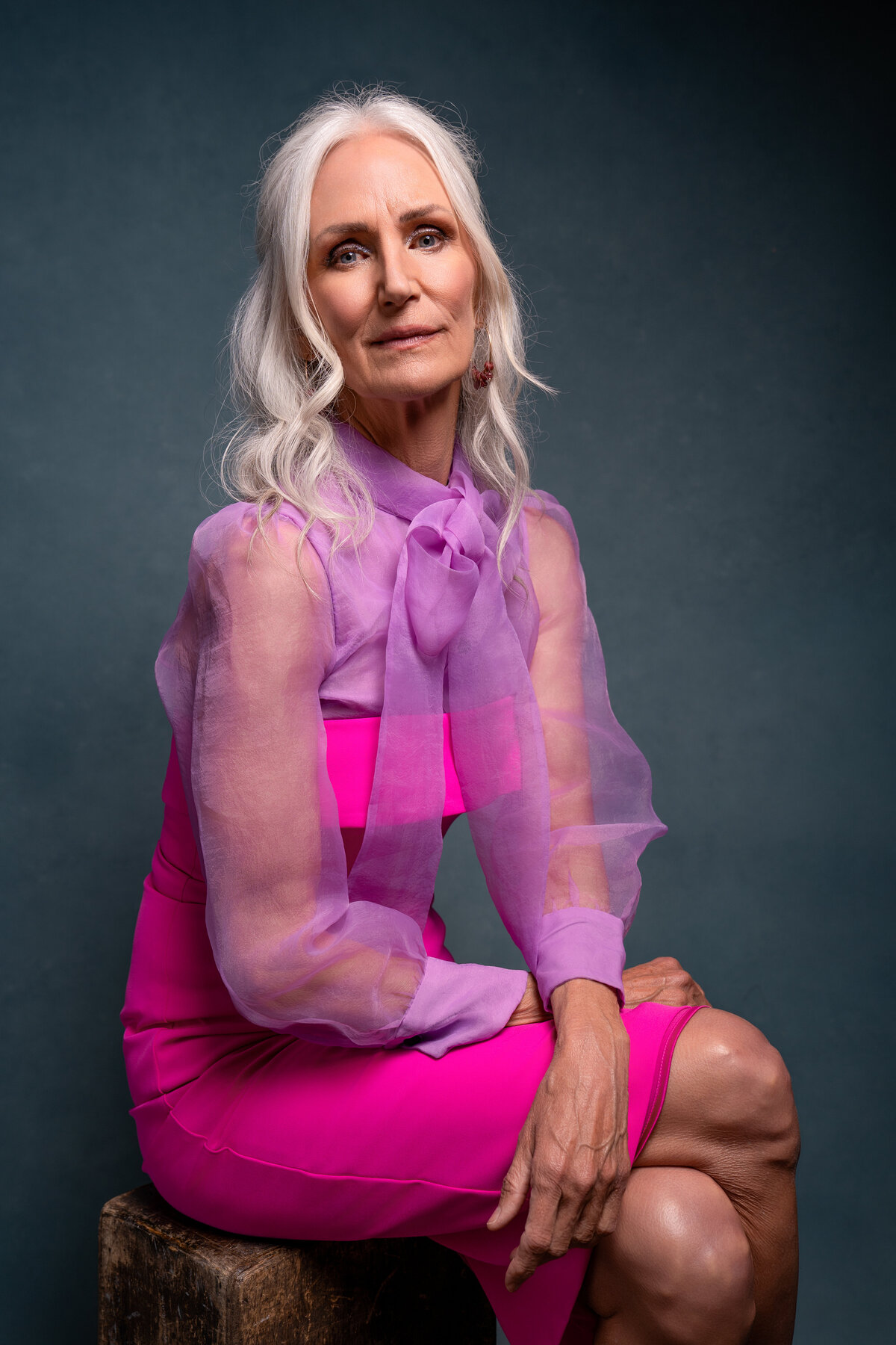 Portrait of middle-aged woman wearing a bright pink and purple dress while sitting down. 