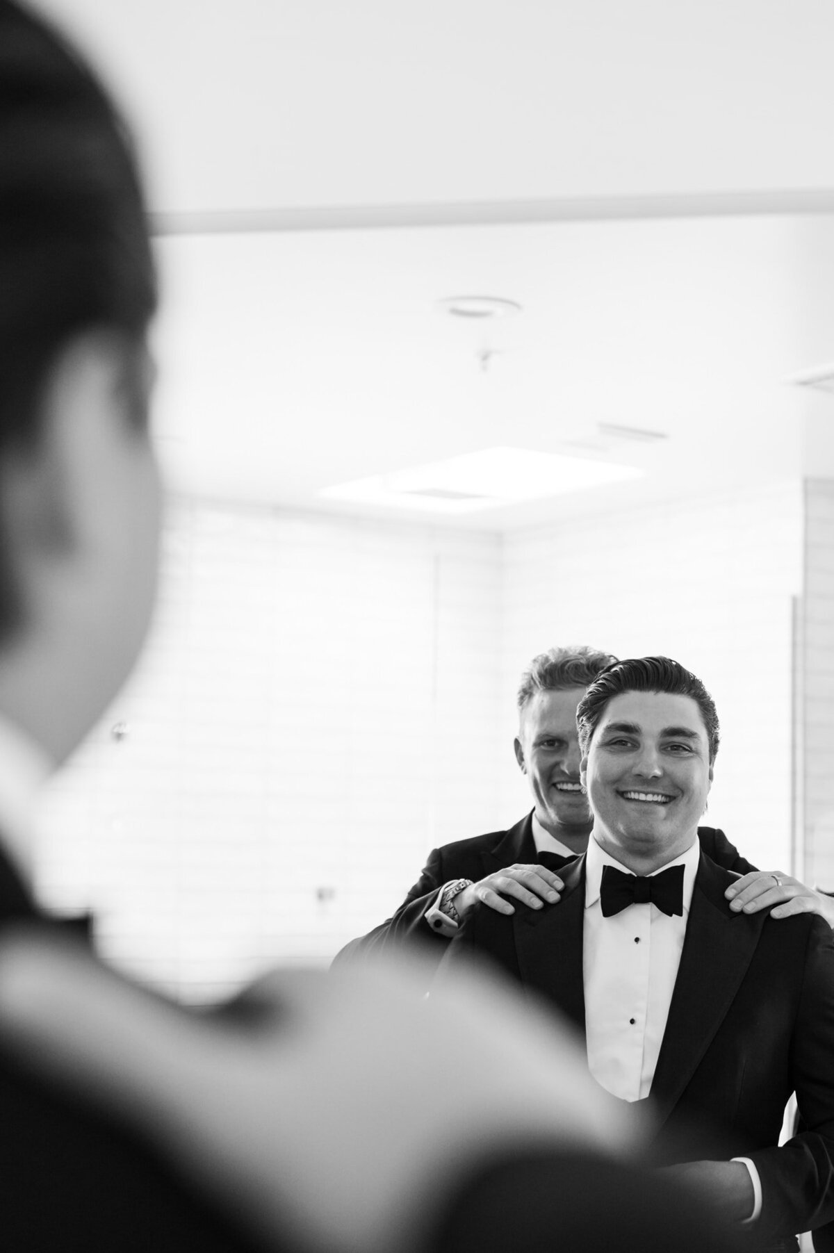 Best man looking in the mirror with groom laughing