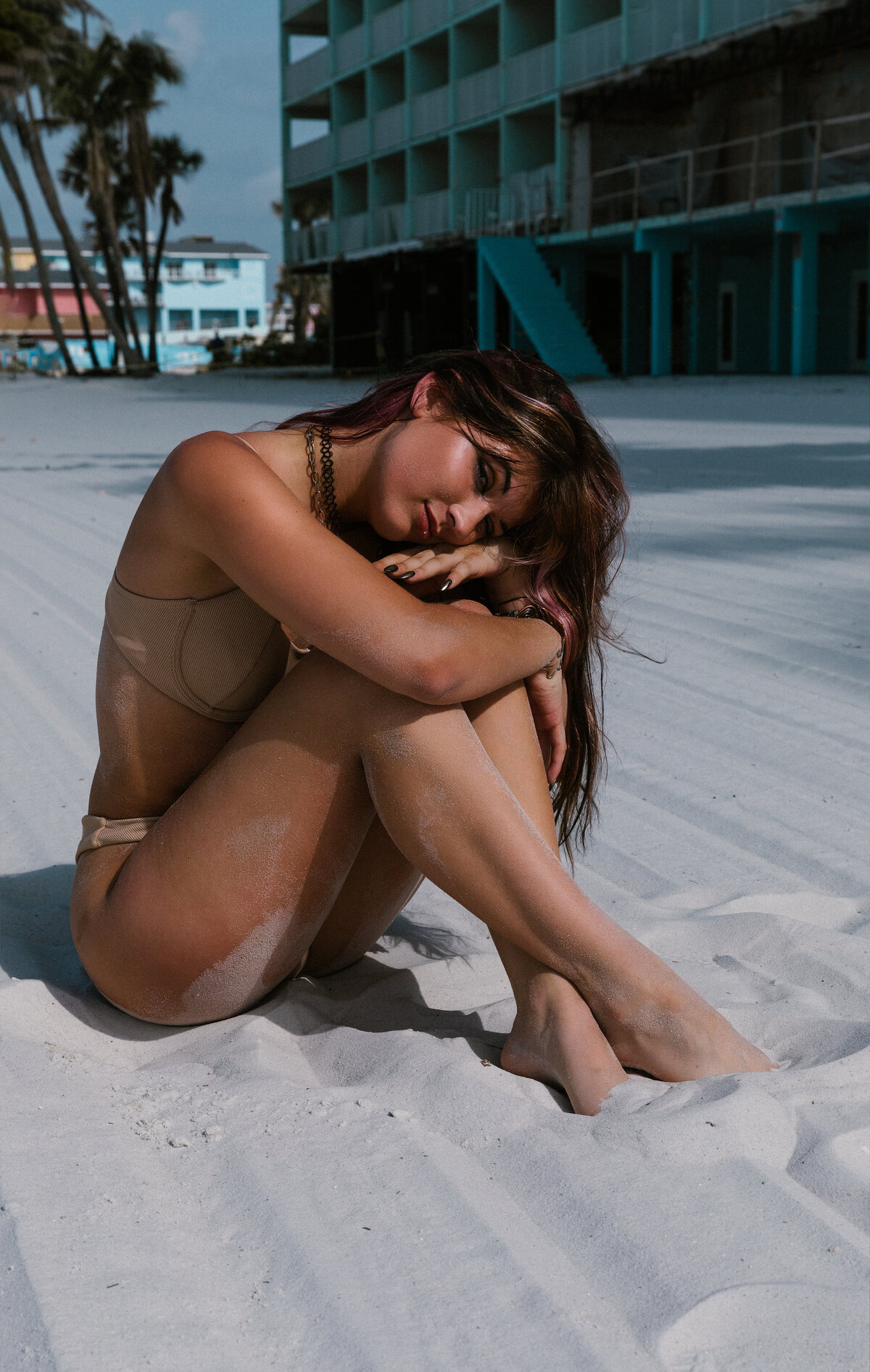 Woman sitting on the beach and resting her head on her knees