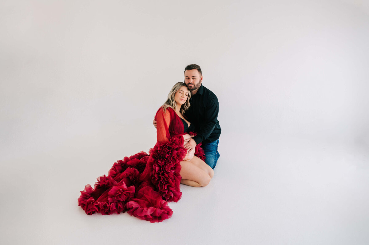 pregnant couple kneeling on floor cuddling in maternity photography studio in Branson