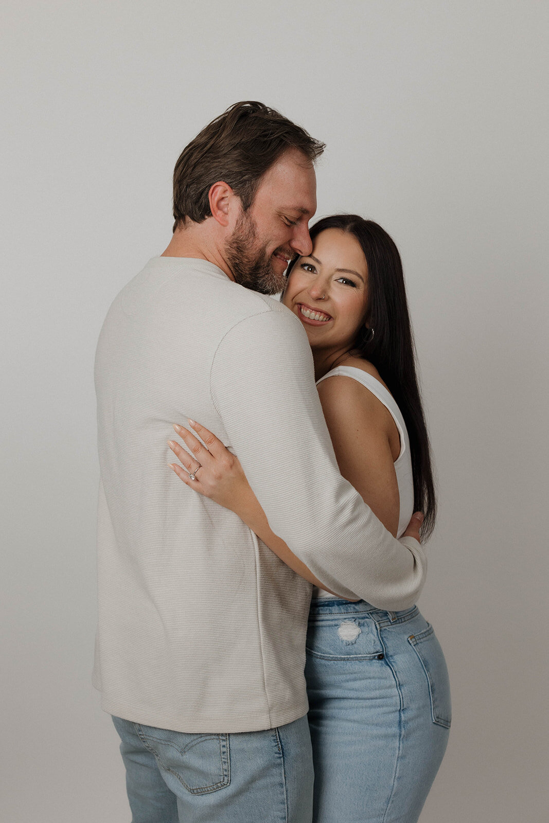 Couple intimately embracing and smiling warmly during their studio engagement photography session, captured by editorial wedding photographers.