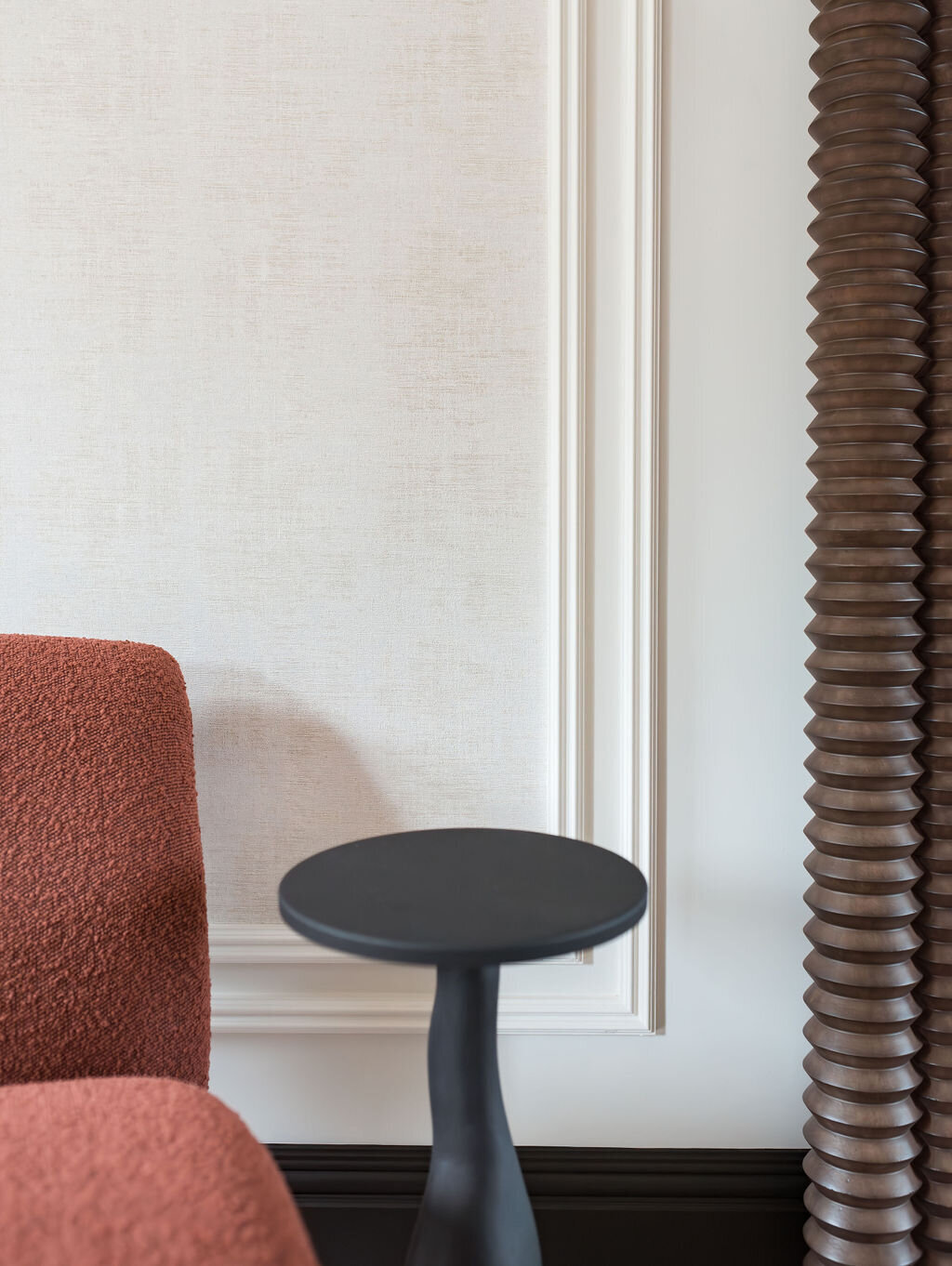 Small black side table next to a red chair in a modern foyer.