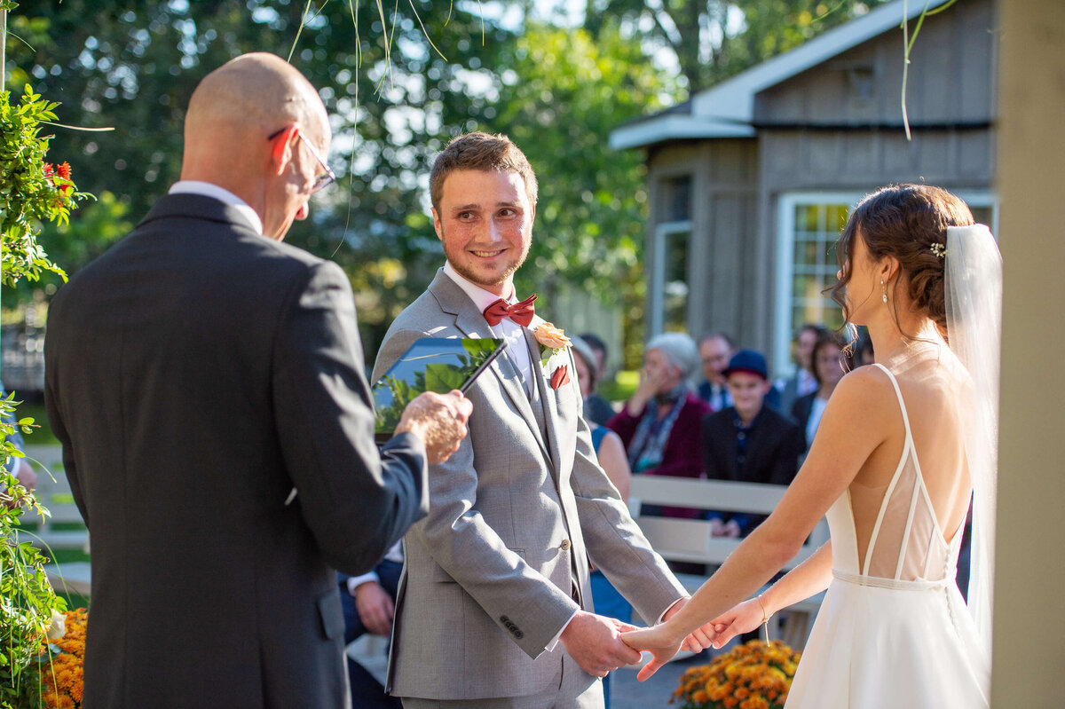 a bride and groom are holding hands smiling at the altar as their officiant recites their vows during their Ottawa wedding at Strathmere venue
