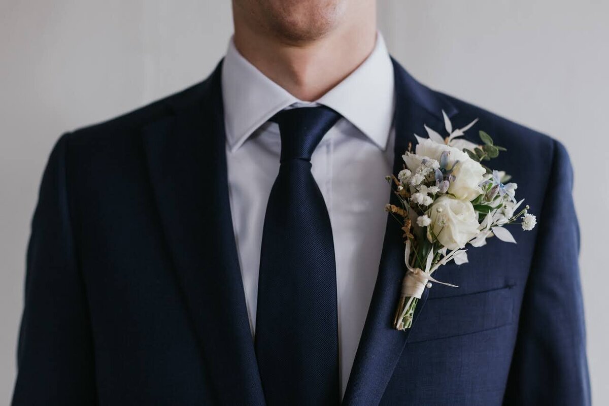 Grooms' boutonniere is pinned onto a blue suit.