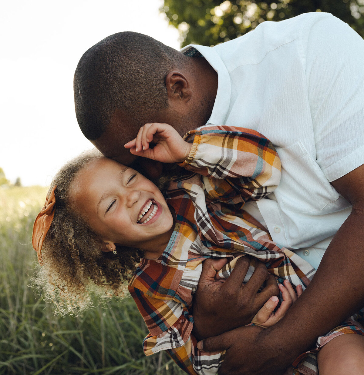 Dad lifting his young daughter into the air as she laughs during a joyful outdoor family photo session