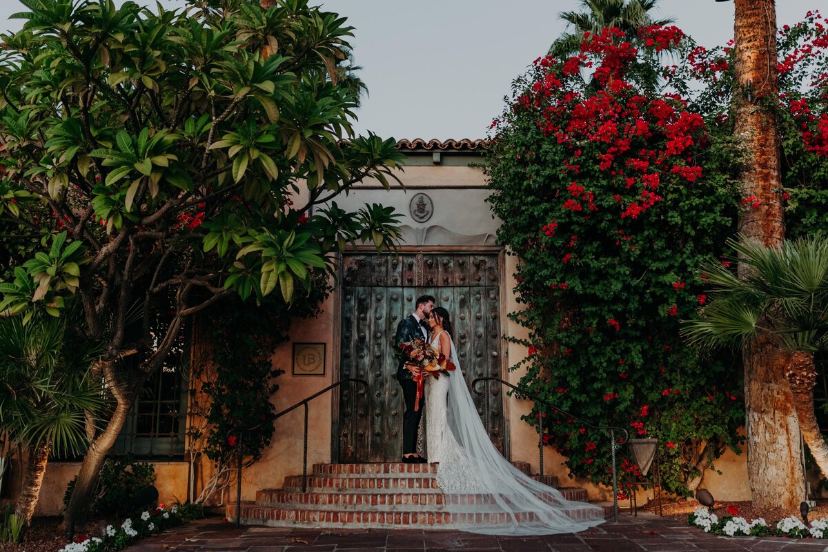 Groom Kisses Bride's Forehead in front of a rustic doorway at the Royal Palms Hotel