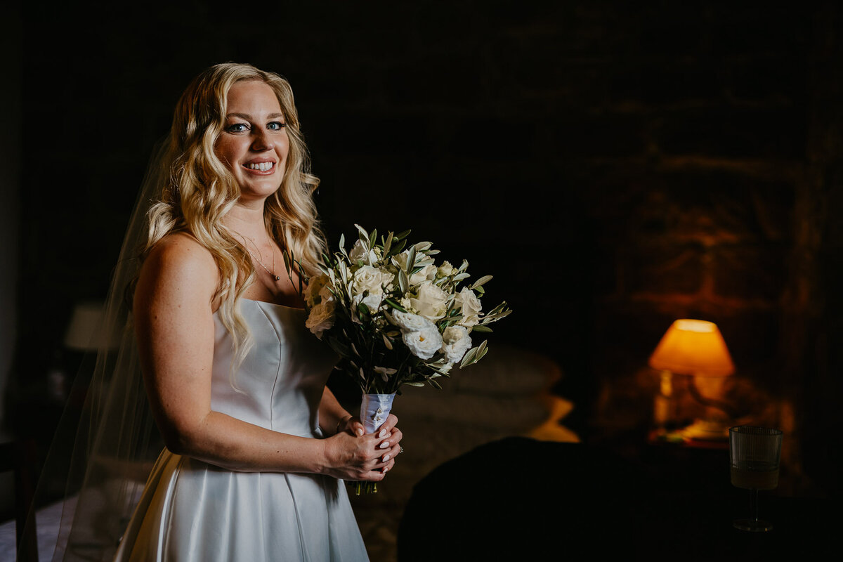 Smiling bride with white flower bouquet at Ristonchi Castle, elegant wedding photographer Florence Tuscany.