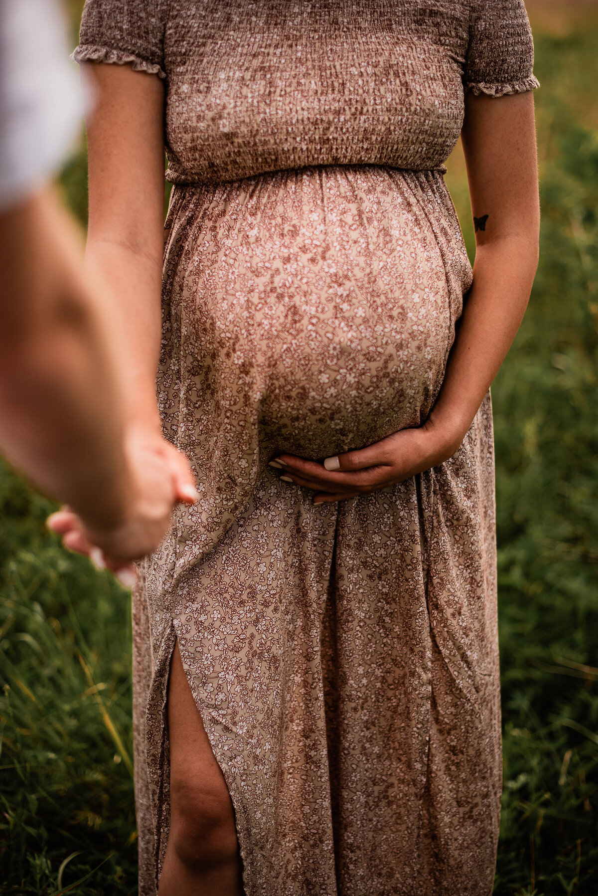 A close up picture of a mom to be holding her belly while wearing a floral dress.