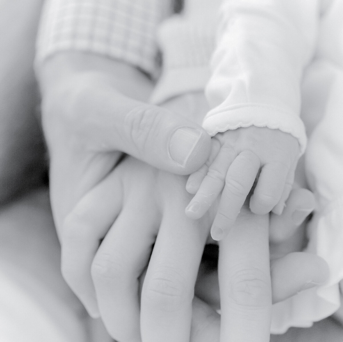 Black and white newborn photography, tiny baby hand holding parents' fingers, Birmingham newborn photographer – A delicate newborn hand grasping the fingers of both parents, symbolizing love, connection, and the beginning of a new life.