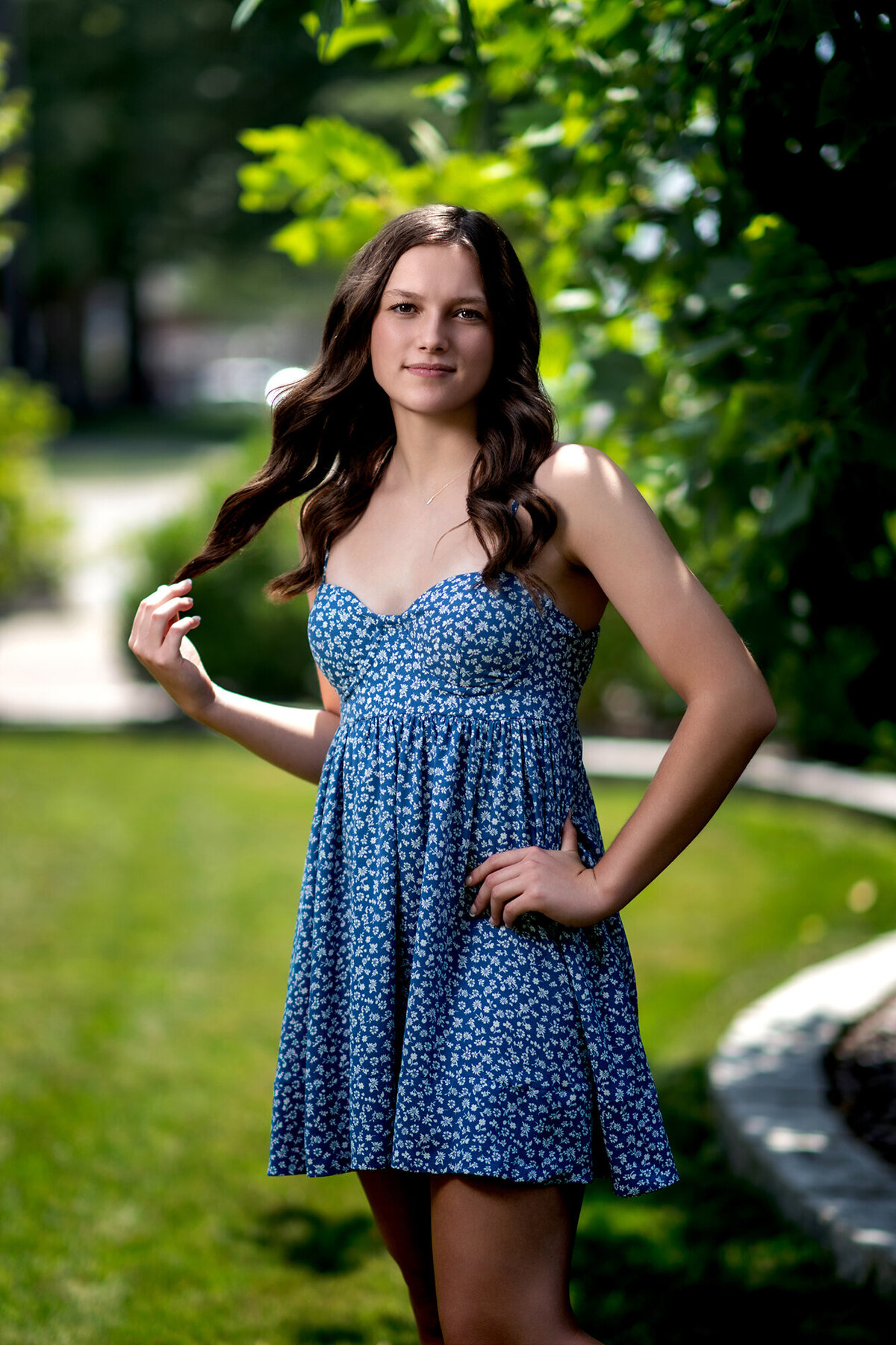 A high school senior twirls her brown hair while standing in a garden in a blue dress for a Pella Senior Photographer