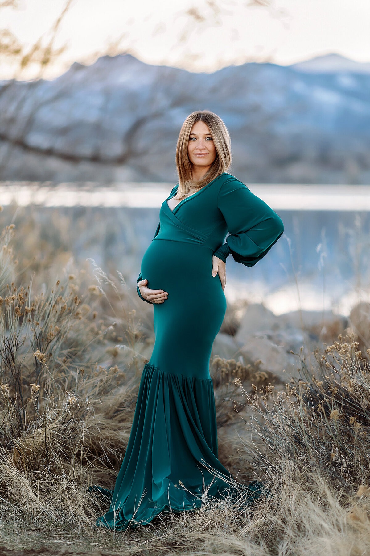 snowy mountain backdrop with mom to be in a green gown for her denver maternity photos