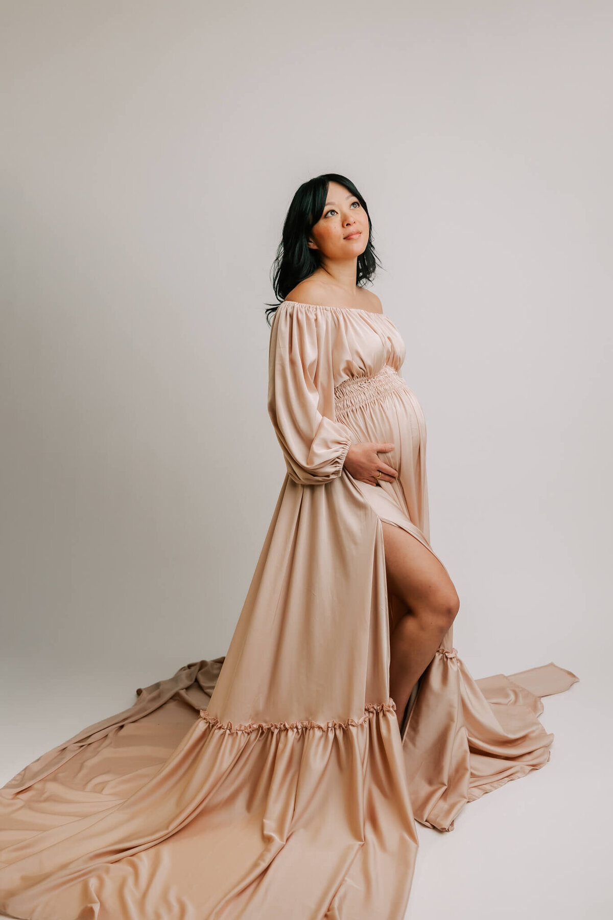 mom holding belly in nude blush satin dress in portland studio maternity session