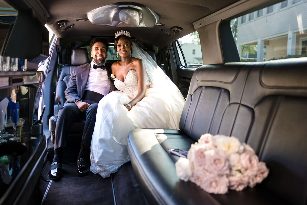 Newlyweds seated in a spacious limousine, the bride in her wedding dress and the groom in a tuxedo, both smiling brightly