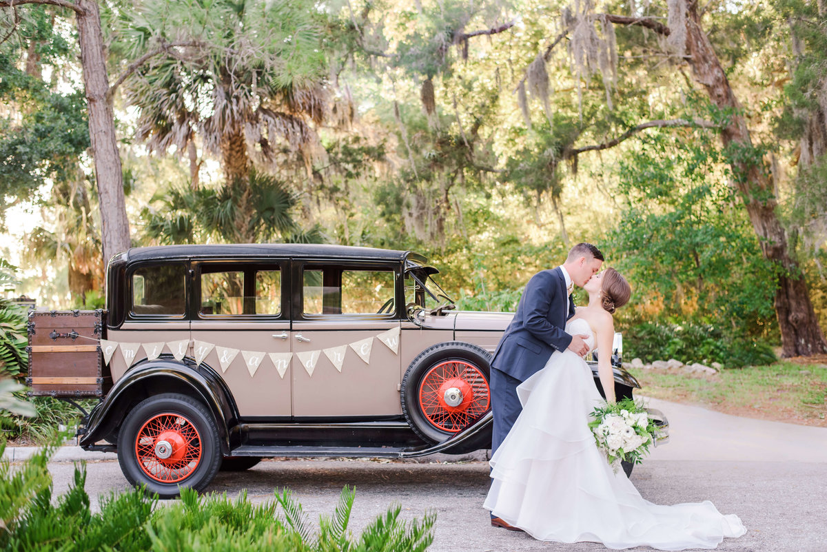 Bride and Groom kiss in front of an Antique car at the Powel Crosley Estate in Florida