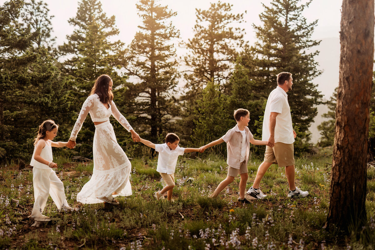 Family of five walking in a horizontal line while holding hands in the rain while walking in the Colorado forests