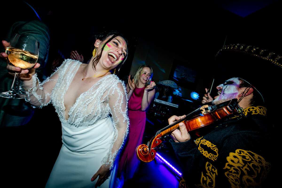 Bride dancing to a mariachi band with a wine glass in her hand and glow in the dark paint stripes on her cheeks..