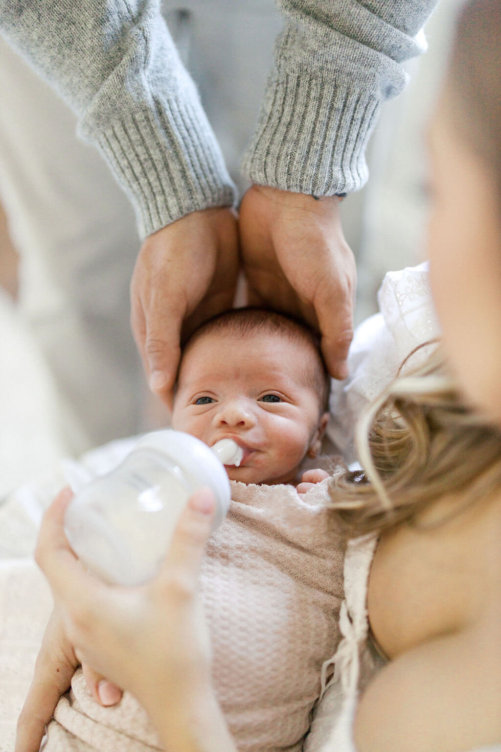 Newborn baby being bottle-fed and gently cradled by parents during in-home lifestyle session in South Florida.