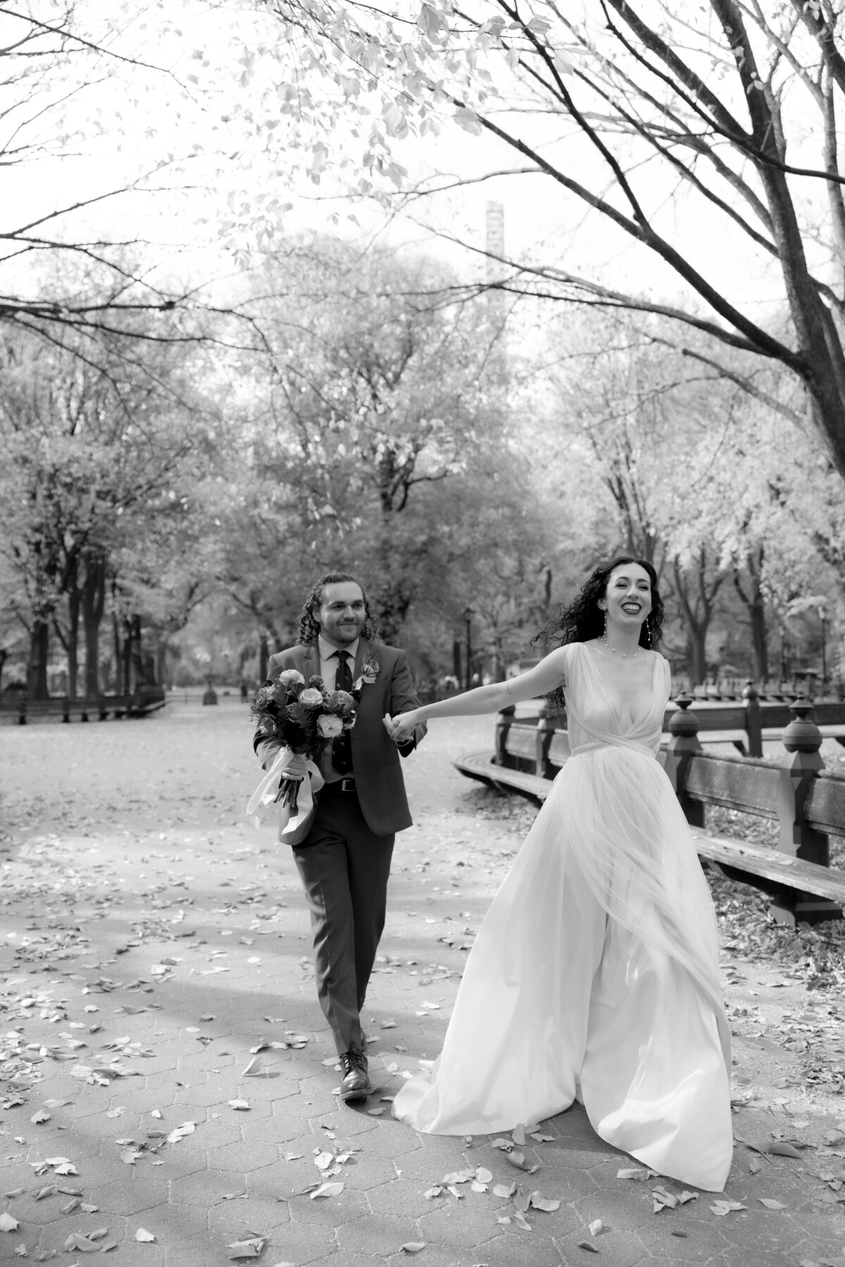 The bride laughing joyfully while holding her bouquet among autumn leaves in Central Park.