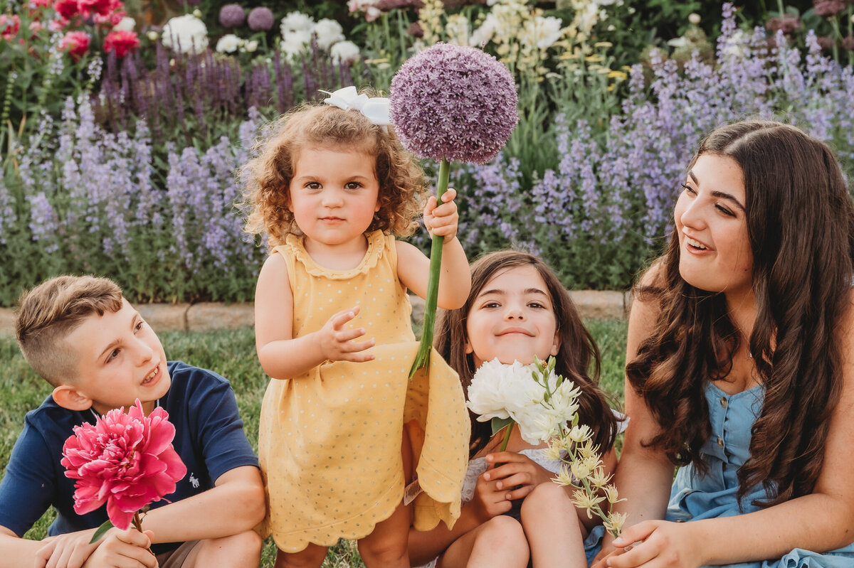 Brother with sisters sitting in grass holding flowers