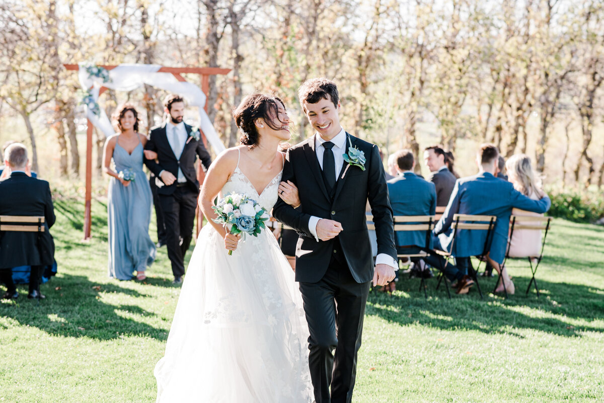 bride holding her grooms arm as they leave their wedding ceremony as she laughs and tlaks with her groom who is smiling captured by denver wedding photographer