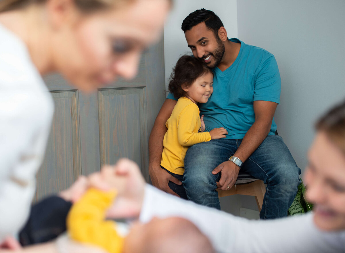 a dad and child smile at their family as their baby is being adjusted by the chiropractor.  Captured by Ottawa Branding Photographer JEMMAN Photography Commercial