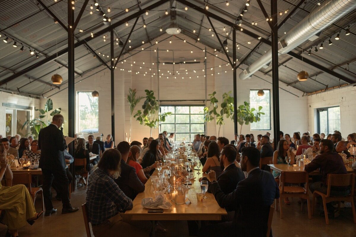 wedding reception guests sit at banquet tables with warm string lighting overhead in image by st paul wedding photographer tom thornton
