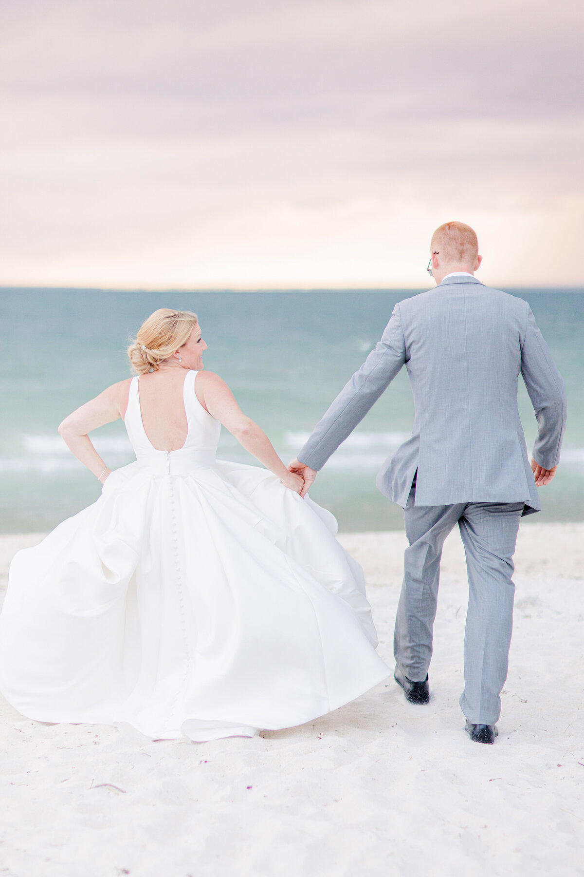 Bride and groom holding hands and running towards the ocean representing a romantic Cape Cod wedding photographer