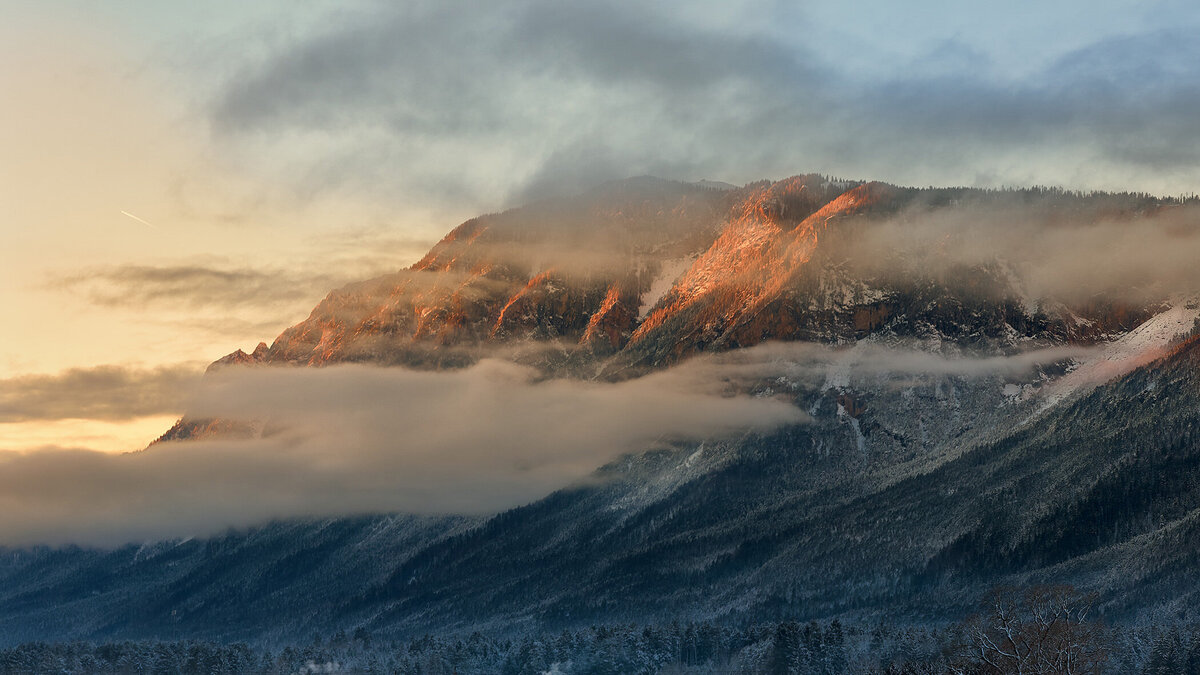 Sonnenaufgang am Dobratsch mit tief hängenden Wolken und rötlich beleuchteten Felswänden – stimmungsvolle Gebirgslandschaft für Natur- und Imagefotografie