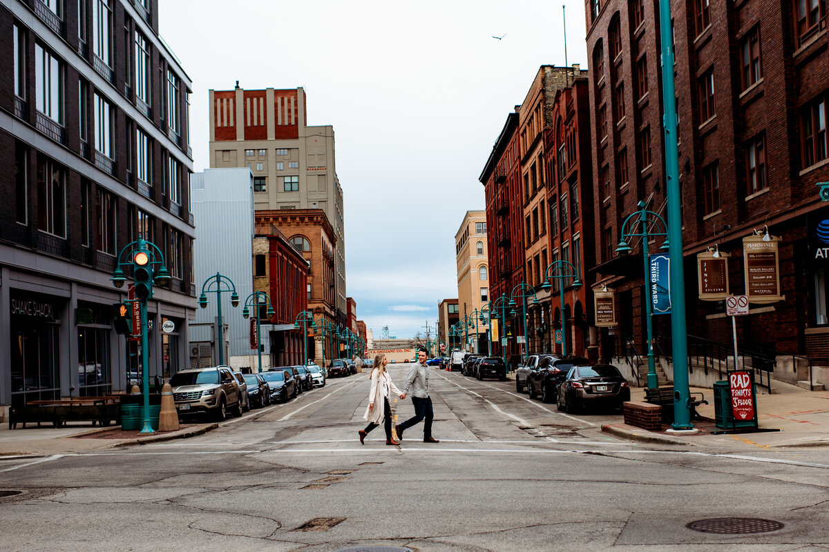 Man and woman holding hands walking across the street in downtown Milwaukee