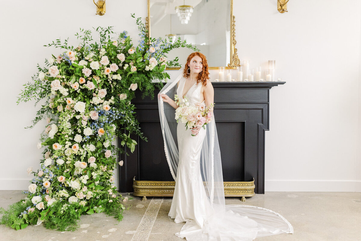 bride smiling and holding her veil while standing in front of a fireplace