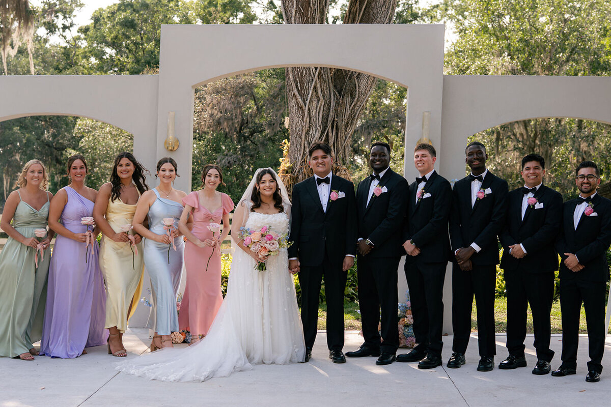 Colorful wedding party celebrating in front of rounded 3 arches ceremony site at Uliana Estate in Lakeland, Florida.
