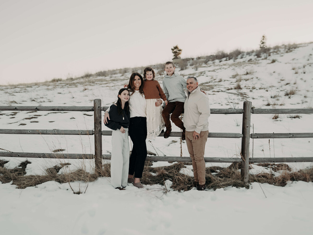 A family of five stylishly, dressed in winter cream, colored clothing poses organically along a fence on a Colorado farm just outside of Denver.