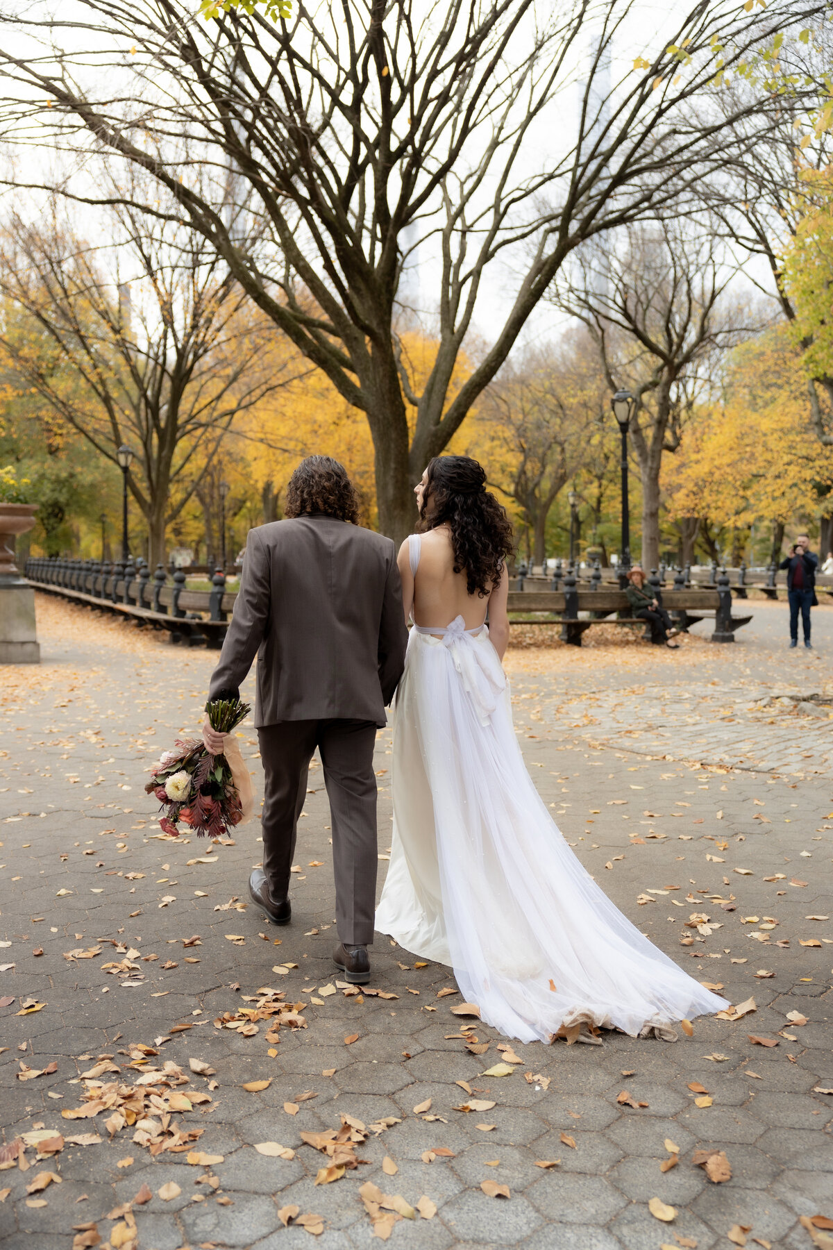The bride laughing joyfully while holding her bouquet among autumn leaves in Central Park.